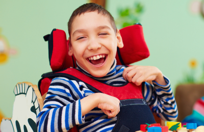 Young white boy in a wheelchair siting at a table with game and smiling.
